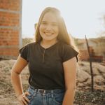 A cheerful young woman stands outdoors at sunset, backlit by warm sunlight.