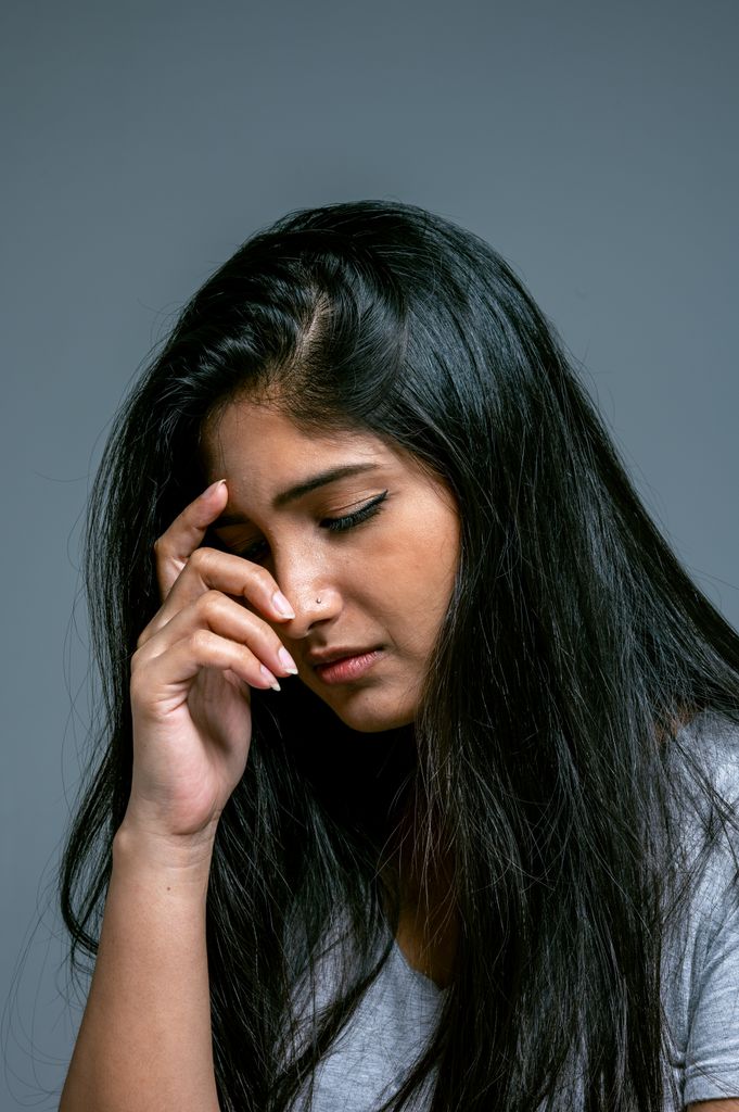 A contemplative woman with long dark hair poses thoughtfully in a studio setting, conveying a mood of introspection.