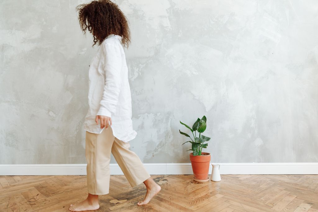 A woman in beige pants walking past a potted plant against a concrete wall.