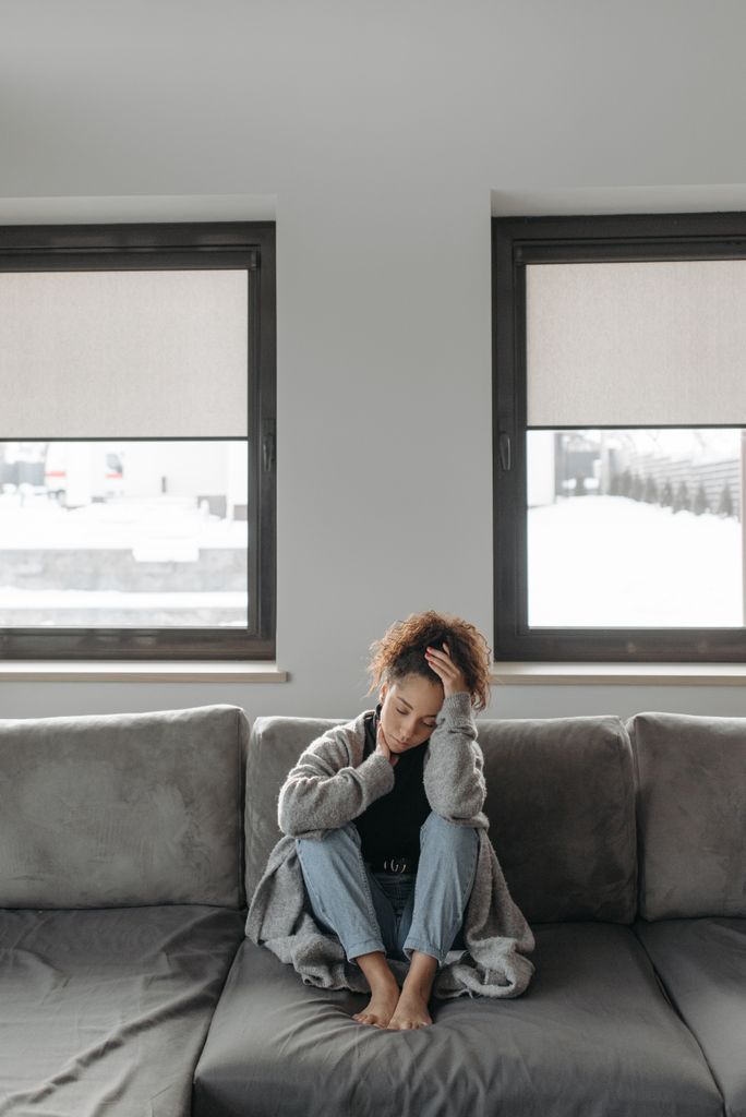 A young woman in a living room feeling unwell, sitting on a gray sofa.