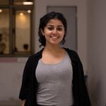 Portrait of a smiling young woman in a black cardigan and gray tank top indoors.