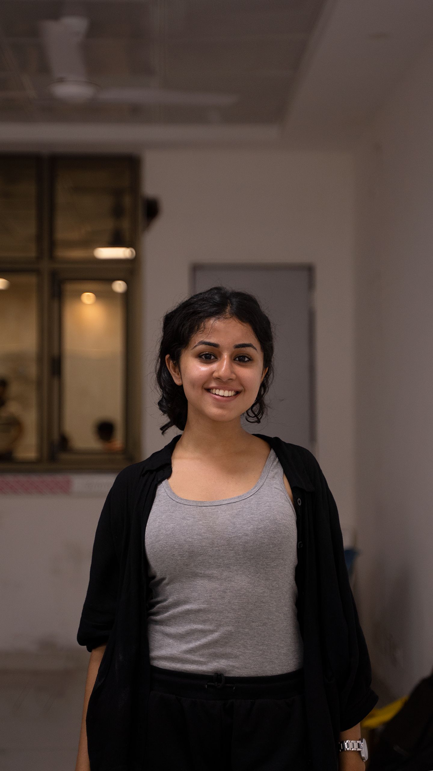 Portrait of a smiling young woman in a black cardigan and gray tank top indoors.
